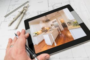 Hand of Architect on Computer Tablet Showing Custom Kitchen Photo Over House Plans, Compass and Ruler.