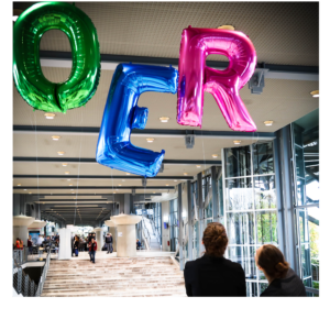 Die Buchstaben OER als bunte schwebende Gasballons oberhalb von zwei aufblickenden Personen. 